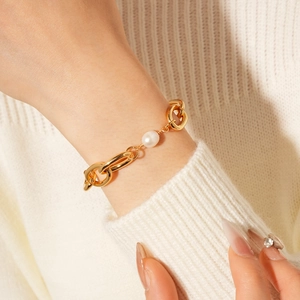 Close-up of a gold chain bracelet with a single freshwater pearl on a beige sweater sleeve
