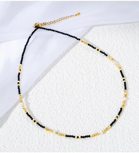 Detail of beaded necklace with black spinel, gold cubes, and white pearls on white veil