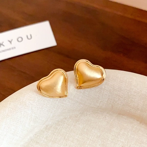 Macro view of heart-shaped gold stud earrings with brushed texture and polished edges