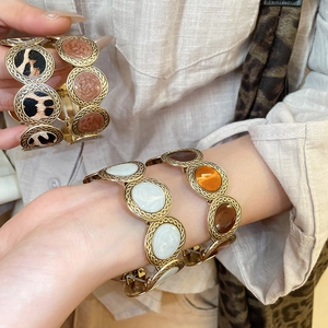 Close-up of leopard print and marble resin inlay details on a golden metal linked bracelet