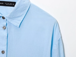 Detail of light blue shirt neckline showing dark buttons and high-quality fabric texture