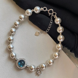 Detail of S925 silver heart charm and blue gemstone on a white pearl bracelet