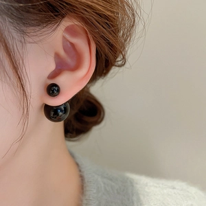 Close-up of elegant double-sided black pearl earrings worn on a model's earlobe