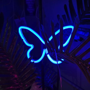 Detailed view of butterfly-shaped blue LED neon light among tropical palm leaves