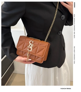 Detail of brown quilted shoulder bag featuring gold 'S' logo and metallic tassels