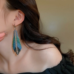Close-up of long feather leaf earrings with blue and green gradient rhinestones on model