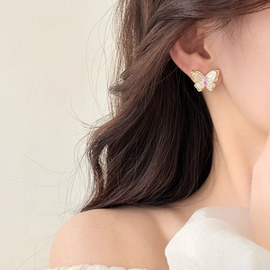 Close-up of model wearing delicate butterfly stud earrings with pearl finish and pink gem