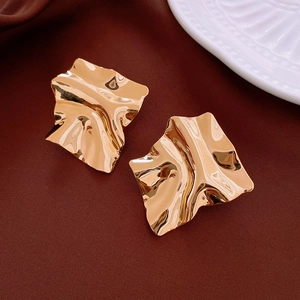 Detailed view of irregular gold plated square earrings on a textured dark fabric backdrop