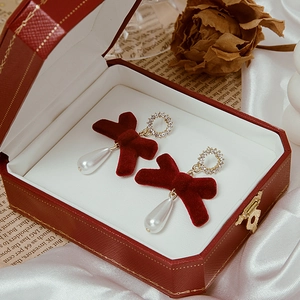 Macro detail of red velvet bow earrings with teardrop pearls on a vintage box