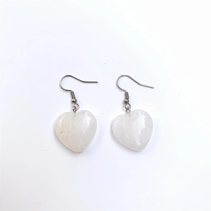 Macro detail of heart-shaped white quartz earrings with silver hooks on white background