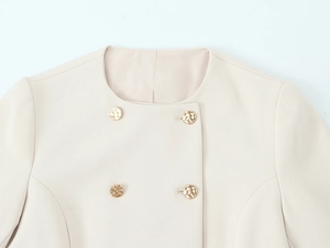 Dettaglio del blazer corto beige con trama a navetta e bottoni in metallo dorato martellato