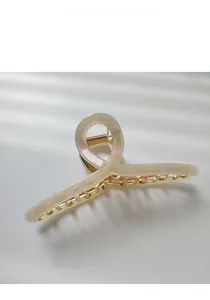 Macro detail of large shell-white resin hair claw clip with golden metal inner frame