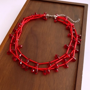 Close-up of red bamboo-style glass beads and teardrop pendant on a layered necklace