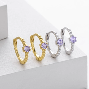 Macro shot of silver and gold huggie hoop earrings with purple zircon and bead texture