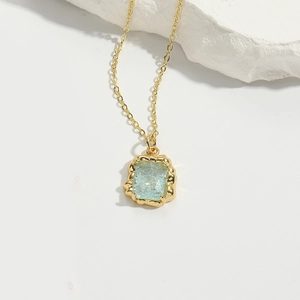 Detail of light blue gemstone pendant with gold wavy base and delicate chain necklace