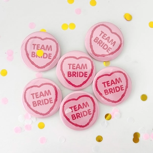 Detail view of 6 pink heart-shaped Team Bride tinplate badges with party confetti