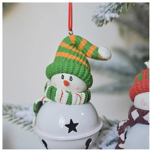 Detail of a snowman Christmas bell ornament with a green and orange knit hat on a snowy tree