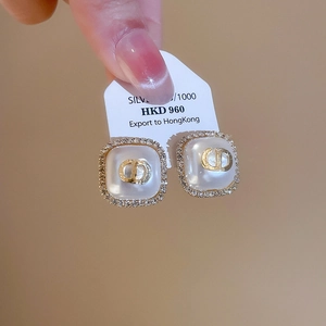 Detail of gold square pearl earrings with rhinestones and CD logo on a white tag