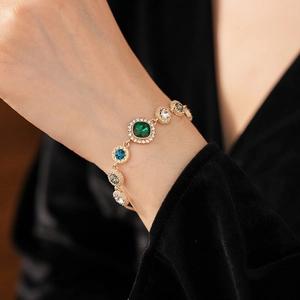 Macro shot of luxury gold chain bracelet with emerald and crystal stones on wrist