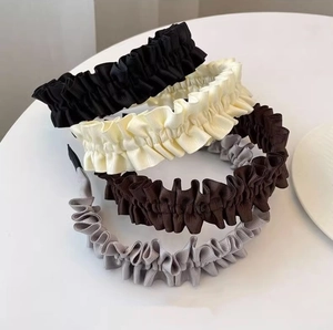 Detail of pleated fabric headbands in black, white, dark brown, and grey on a round table