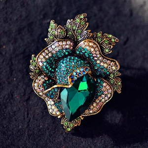 Close-up of a floral brooch featuring a large teardrop emerald crystal and vintage gold leaves