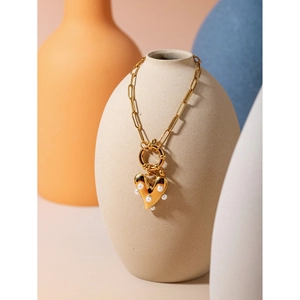 Close-up of golden heart pendant with pearls on a textured link chain over a ceramic vase