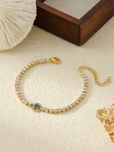 Detail of gold-plated tennis bracelet with blue central stone and sparkling cubic zirconia