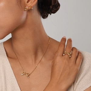 Detailed view of 18k gold plated stainless steel bow necklace and earrings on model