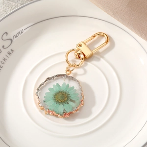 Floral resin keychain featuring a mint daisy in a gold-edged circular charm on a white tray