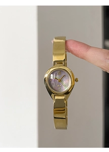 Close-up of golden teardrop watch with purple mother-of-pearl dial and Roman numerals