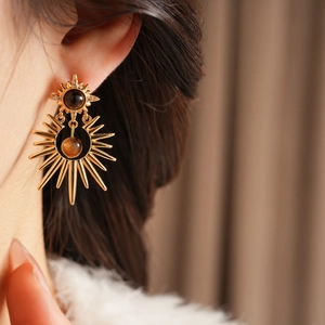 Close-up of golden sunburst earrings with amber stones and zircons on a model's ear