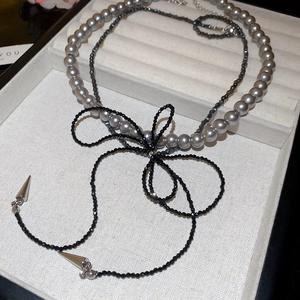 Detail of double-layer necklace with grey pearls, black crystal beads, and bow design