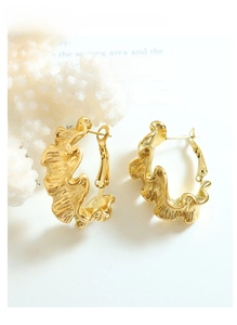 Détail de boucles d'oreilles dorées ondulées avec plis irréguliers sur corail blanc