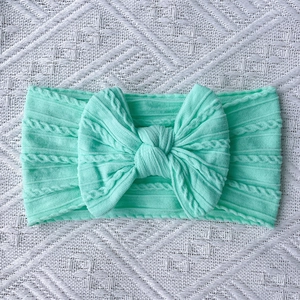 Detailed close-up of mint green cable knit baby headband with a large soft bow decoration