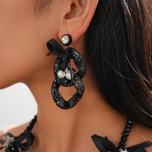 Detail of chunky black chain earring with white ink splatters, bow, and faux pearls