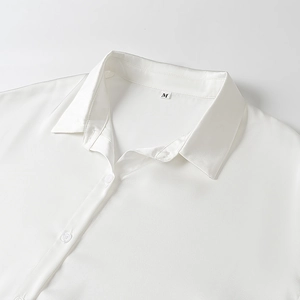 Détail du col d'une chemise en satin blanc montrant la texture lisse et le bouton discret