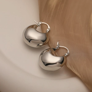 Polished silver teardrop hoop earrings on white ceramic and gold silk background