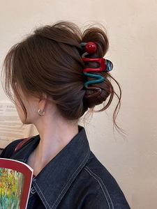 Detail of wavy colorful hair claw clip with red decorative ball for bun styling