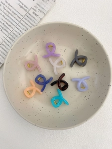 Close-up of colorful translucent mini claw clips in a ceramic bowl with gold springs