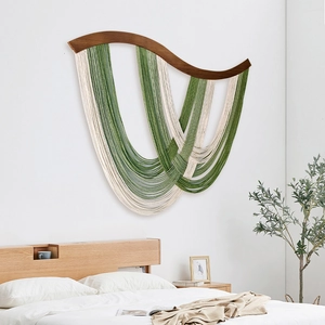 Moderner Boho Wandbehang mit gebogenem dunklem Holzbalken und grünen Quasten Deko