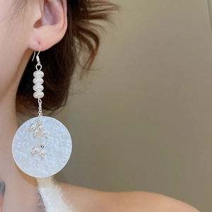 Close-up of pearl drop earrings with round shell charms on a model for elegant styling