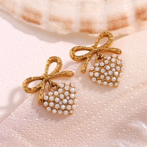Macro detail of gold bow and heart pearl earrings on a fresh textured background