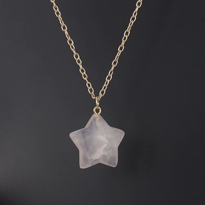Detailed close-up of a pink crystal star pendant on a gold chain over black background