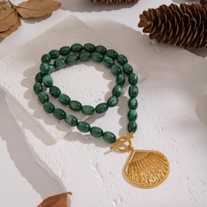 Vintage green beaded necklace with large gold shell pendant on stone display