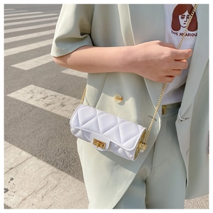 Close-up of a white quilted cylinder bag with gold chain strap on a street scene