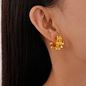 Close-up of a model wearing a layered golden floral C-shape hoop earring with metallic finish