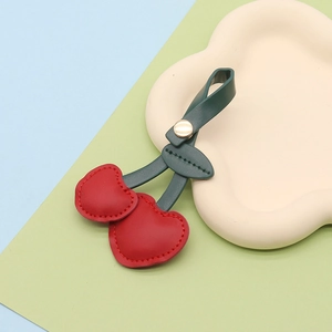 Detailed close-up of a red leather cherry keychain charm on a cloud-shaped tray