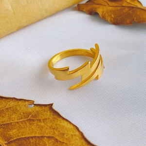 Minimalist golden lightning bolt open ring on white fabric with autumn leaves