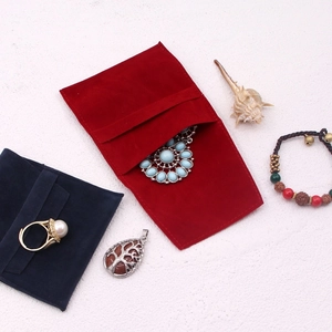Flat lay of red and dark blue suede jewelry pouches with rings and pendants on white background