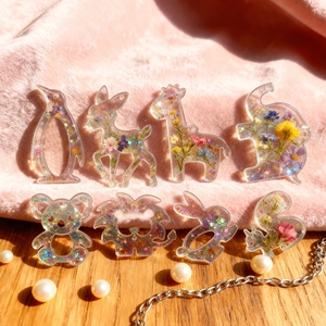 Détail de 8 pendentifs animaux en résine avec fleurs séchées sur fond en fourrure rose